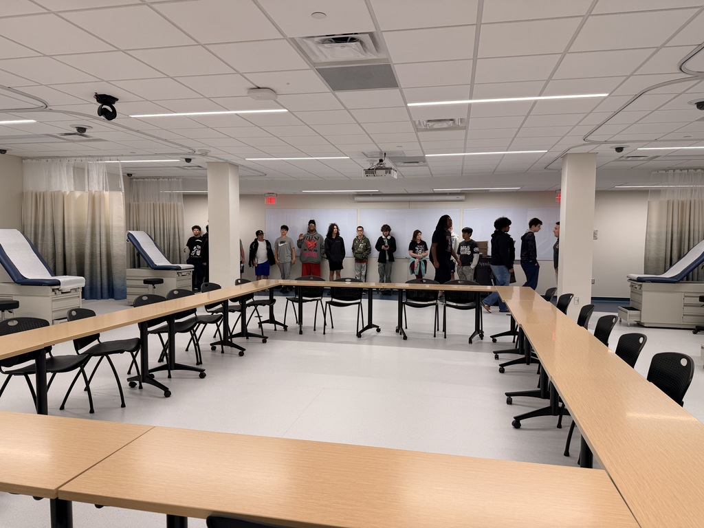 A room with a long table, chairs, and people standing. A large white pillar in the center.