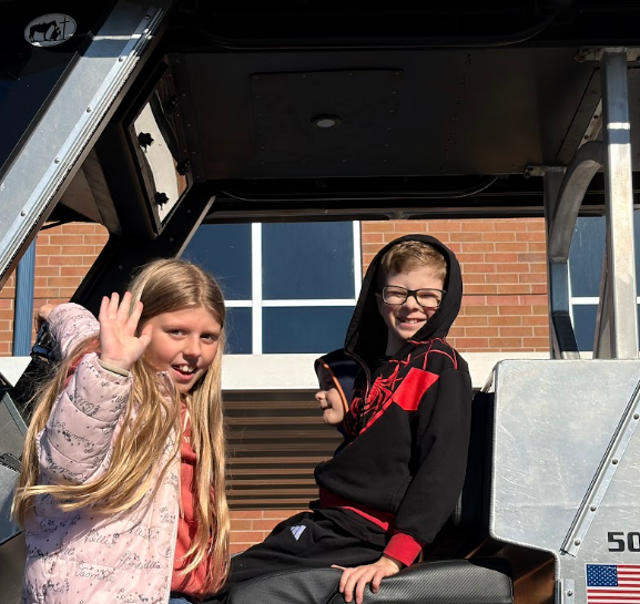 Two children sit inside a vehicle with the number 50 visible on the side. One waves.