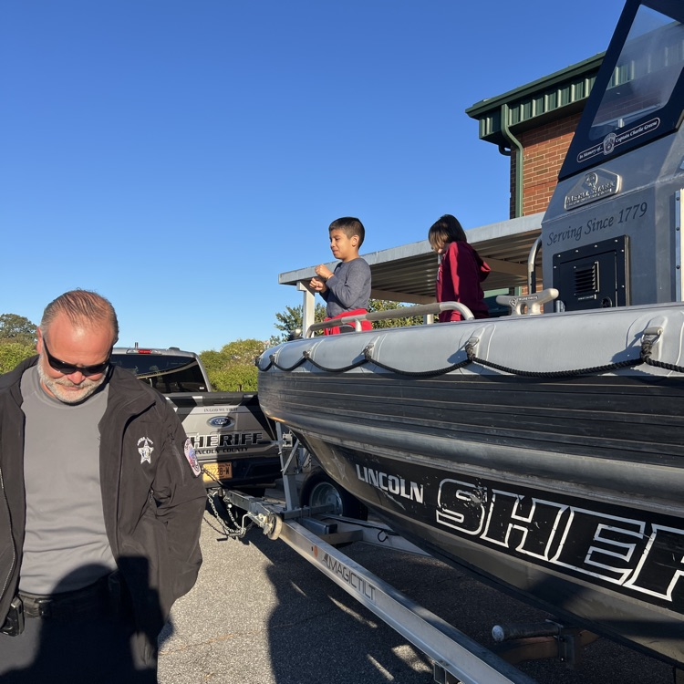 Adult man stands by trailer; child and adult on boat with words "Lincoln Sheriff" on side.