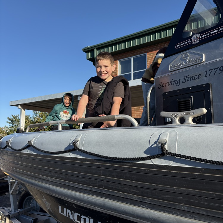 A child stands on a boat with a railing in front of a building.
