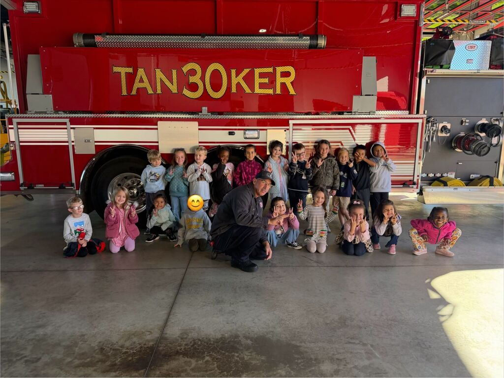 Children in winter wear pose with a firefighter in front of a fire truck.