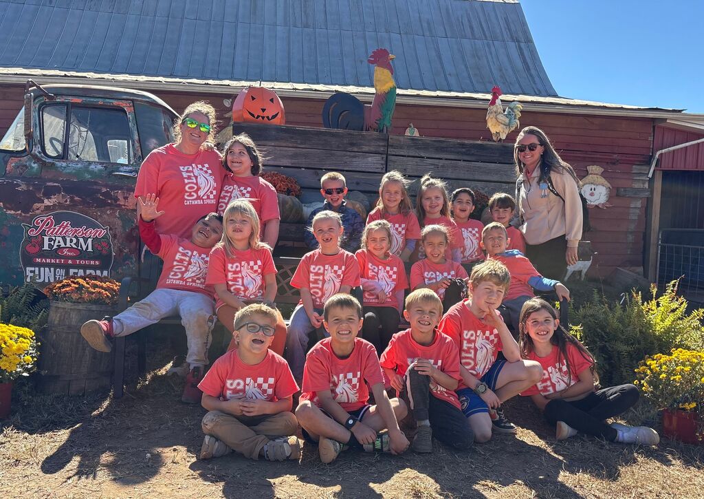 Children and adults in orange shirts pose for a photo in front of a farm building.