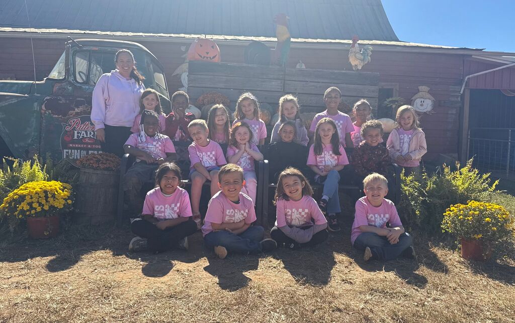 A group of children in pink shirts poses for a photo in front of a building.