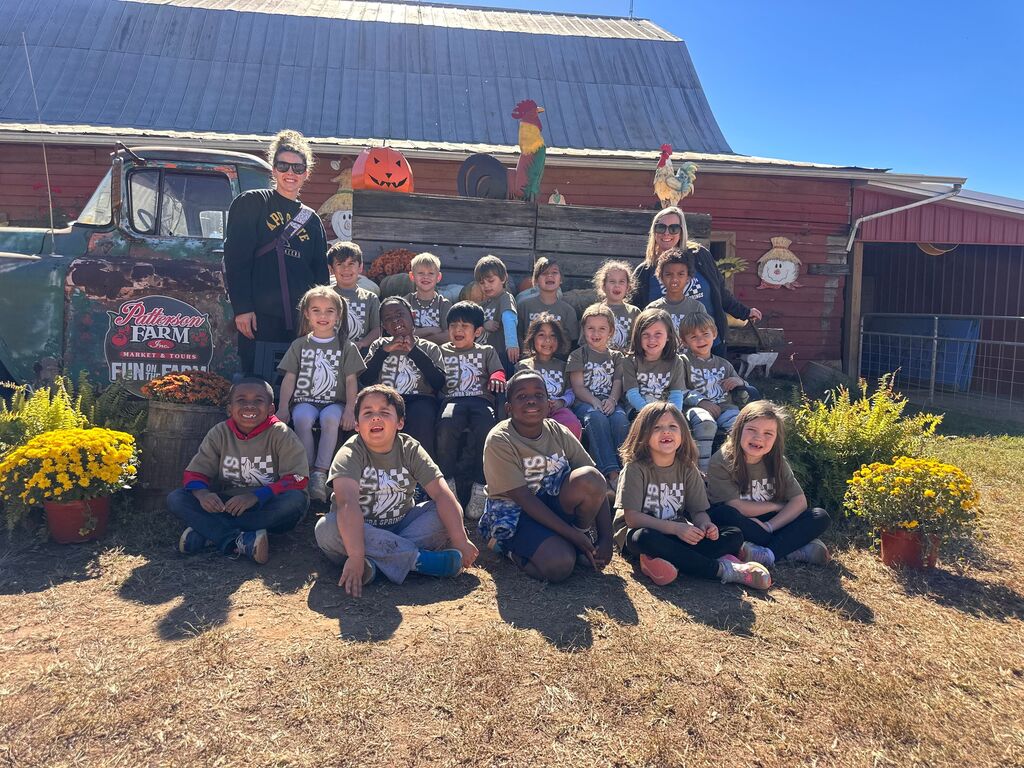 Group of children in matching shirts posing for a photo on a dirt path in front of a barn.