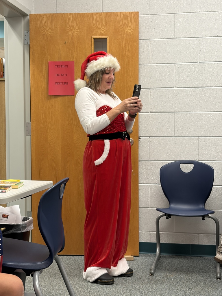 Woman in red Santa suit with white hat holding phone in front of a door.