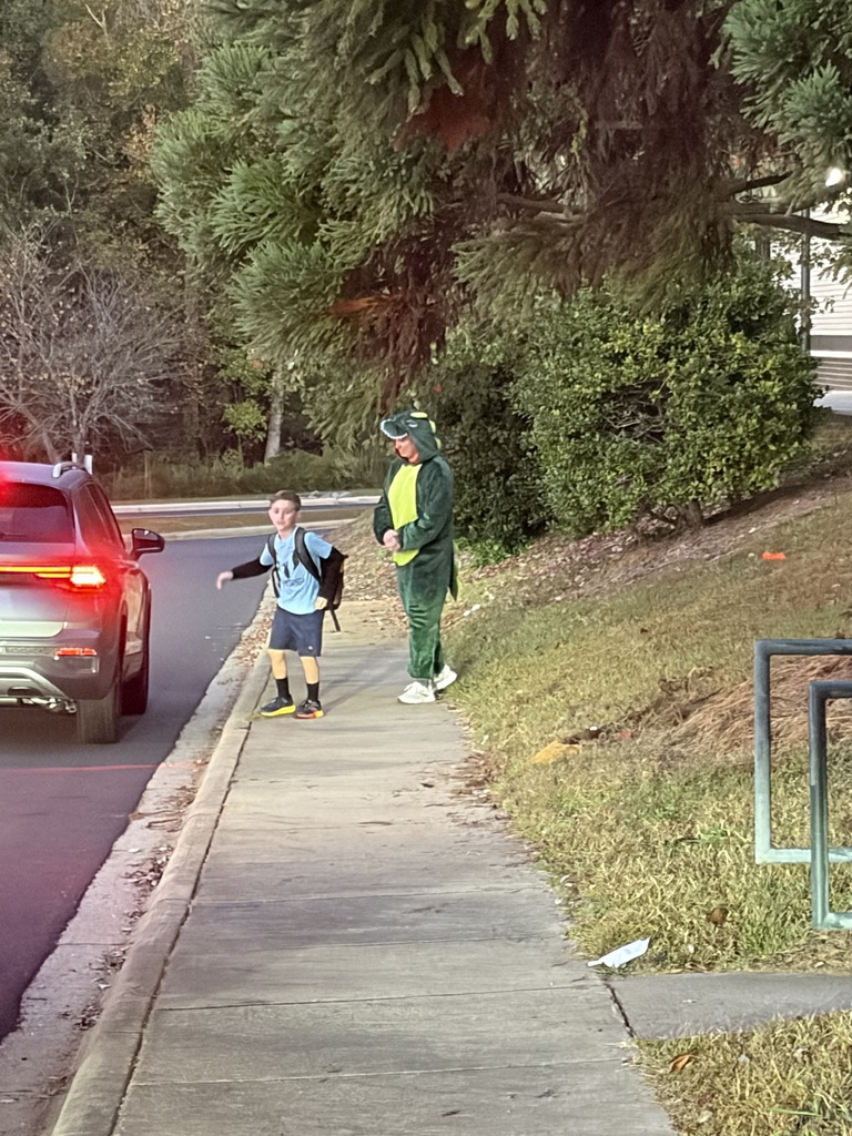 A child in a backpack crossing the street with an adult on a sidewalk.