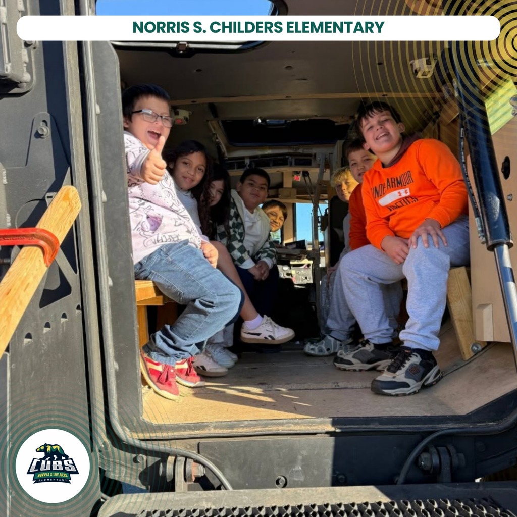 Kids sit inside the back of a bus, smiling, wearing glasses, sneakers, and orange shirts.
