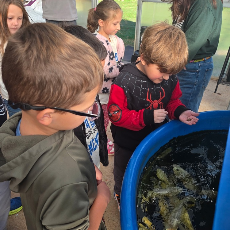 A group of children and adults observe fish in a blue tank, with some children wearing glasses.