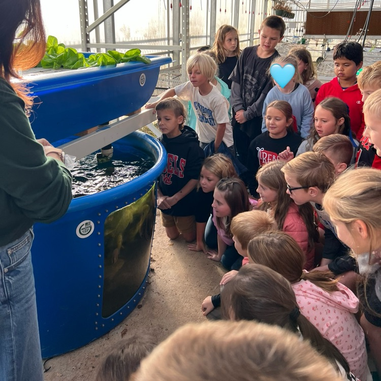 An adult showing an indoor fish tank to students gathered around it, some with glasses.