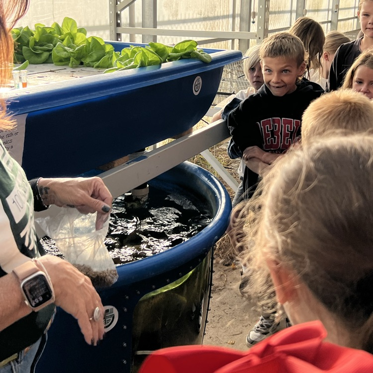 Group of students and adults outside near blue bins; plants in one bin, water in another.
