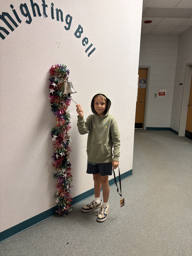 A child holds a bell attached to a decorative garland on a wall with text.