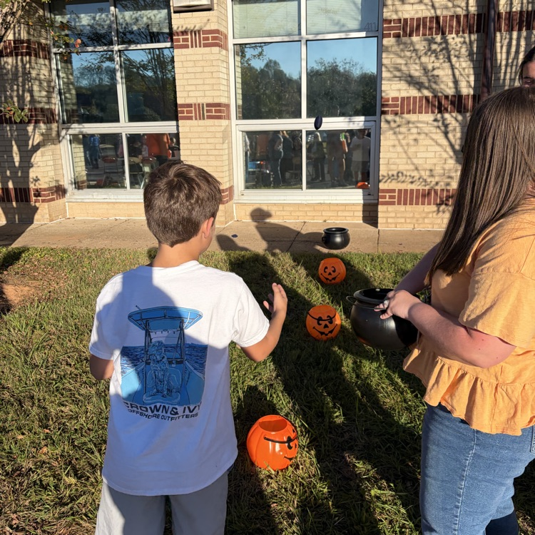 A boy and a woman in front of a building, with pumpkins on the grass.