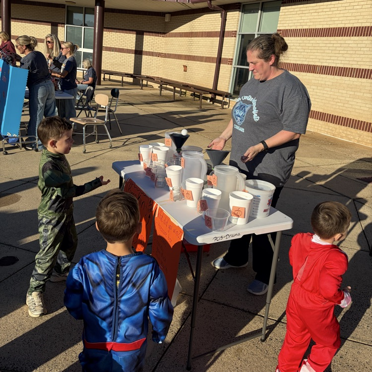 Woman standing behind a table with pitchers, cups, and bowls with kids standing in front.