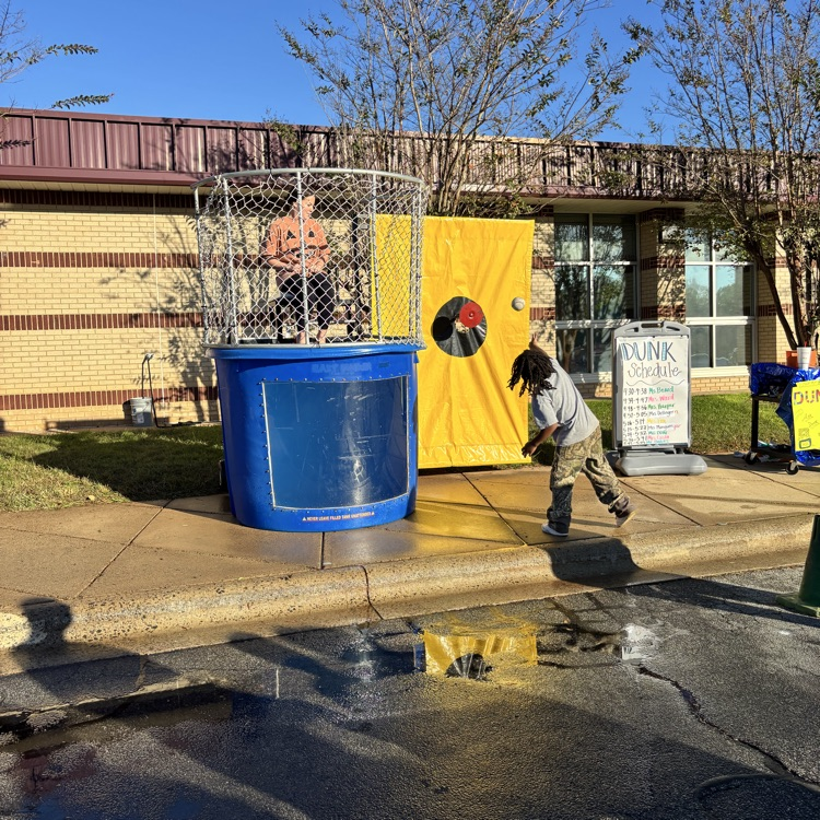 A child in a jacket throws a ball into a large blue container with a target on it.