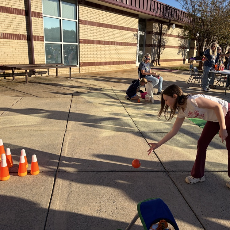 A person throws a ball toward orange cones set up on a sidewalk near a building.