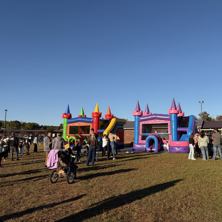People walking around inflatable bounce houses on a grass field, a building in the background.