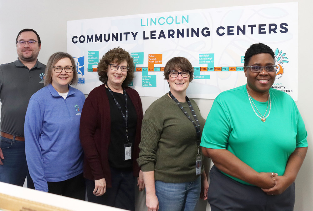 Five Lincoln Community Learning Centers employees are standing in front of a Lincoln CLC banner that is hanging on one of the walls of their new office. From left, Mark Tackett, Nola Derby-Bennett, Brooke Rudeen, Samantha Cressler and Irene Prince; not pictured, Kristi Chambers and Kate Sydik.