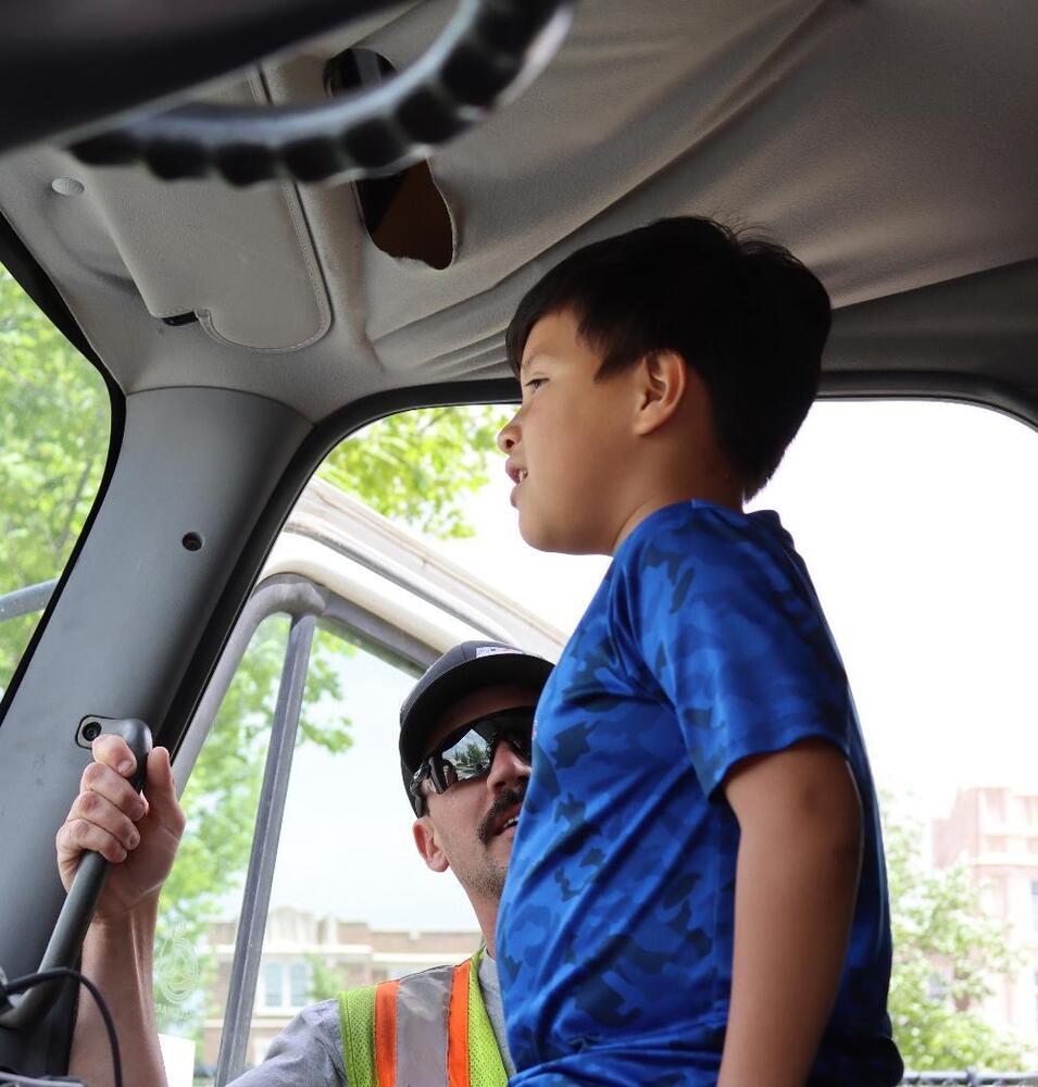 A boy observes a man operating a vehicle's gear shift; they are seated inside a truck cab.