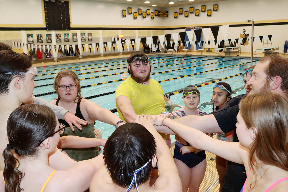 Ten swimmers and coaches in Southeast High School's inclusive swimming program put their hands together for a high five while standing next to the school swimming pool.
