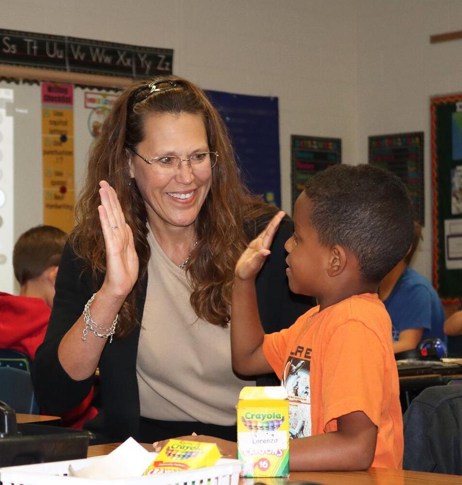 Cavett Elementary School Principal Kathleen Dering prepares to give a high-five to a student after helping her off the bus.