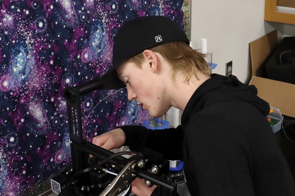 A Lincoln High student fixes a machine in his classroom. He is adjusting part of the machine with his right hand.