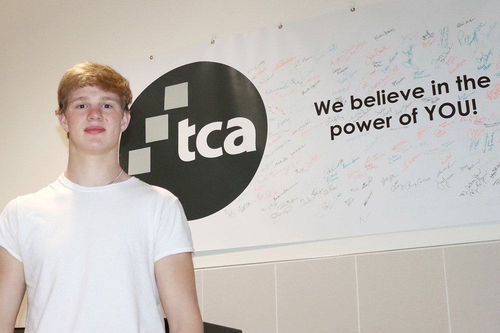 The Career Academy senior Eric stands in front of a poster that has TCA's logo on it. The poster reads “We believe in the power of you” and has more than 50 signatures on it in different colors of ink.