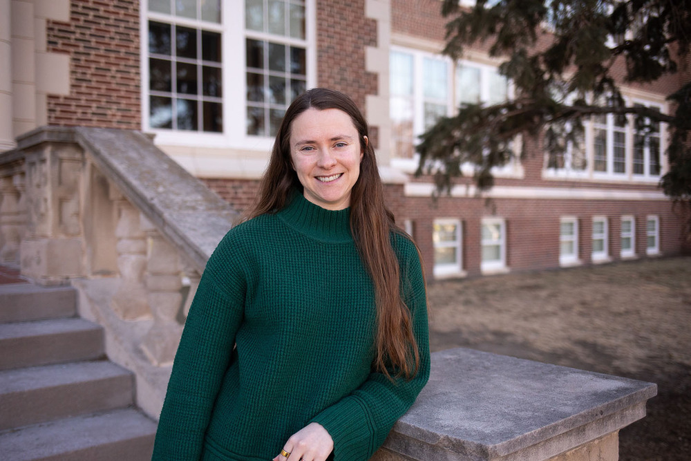 Sara Gahan smiles as she stands outside the front stone steps of a school building. She is leaning up against a railing of Prescott Elementary School.