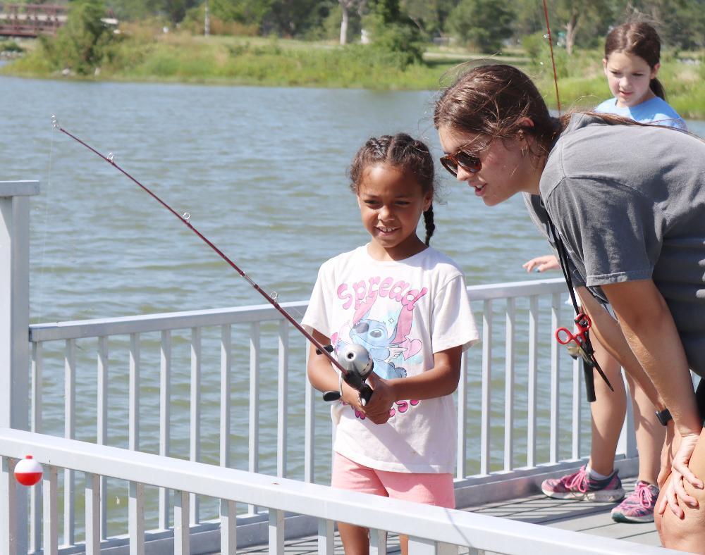 Outdoor Explorers Club student Daisha smiles as she holds her fishing rod over the ledge of a dock at a summer enrichment club activity at Arnold CLC.