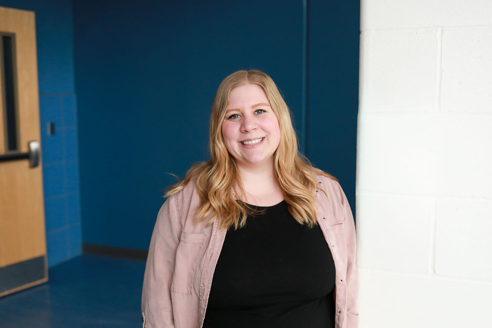 Emily Nathan smiles in a hallway at The Career Academy. There is a door on the far lefthand side of the photo.