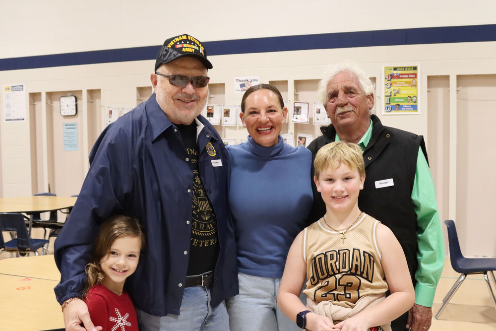 Three adults and two students are standing in a group in Riley Elementary School's cafeteria. All five people are smiling.