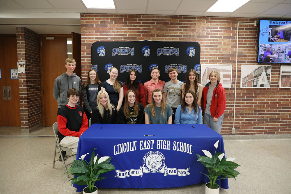Thirteen East High School seniors smile in a group photo during a signing ceremony for future educators. Five girls are sitting in the front row and five girls and two boys are standing in the back row.
