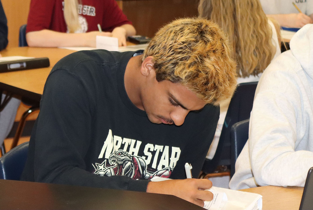 A North Star High School student concentrates as he takes notes with a pencil. He is facing left to right and is sitting at a table.