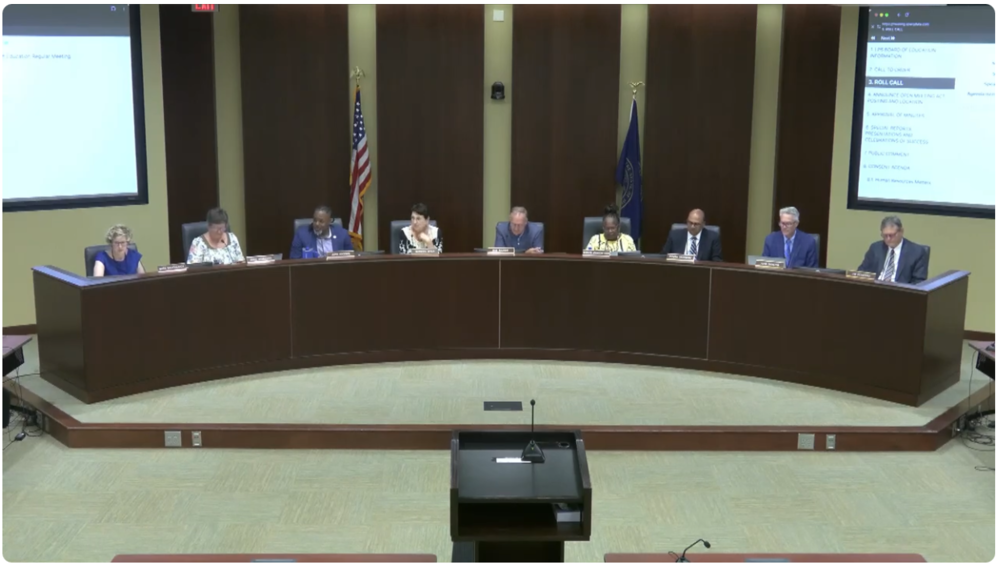 The seven members of the Board of Education, the Superintendent, and the Lawyer sitting at the Board dias.