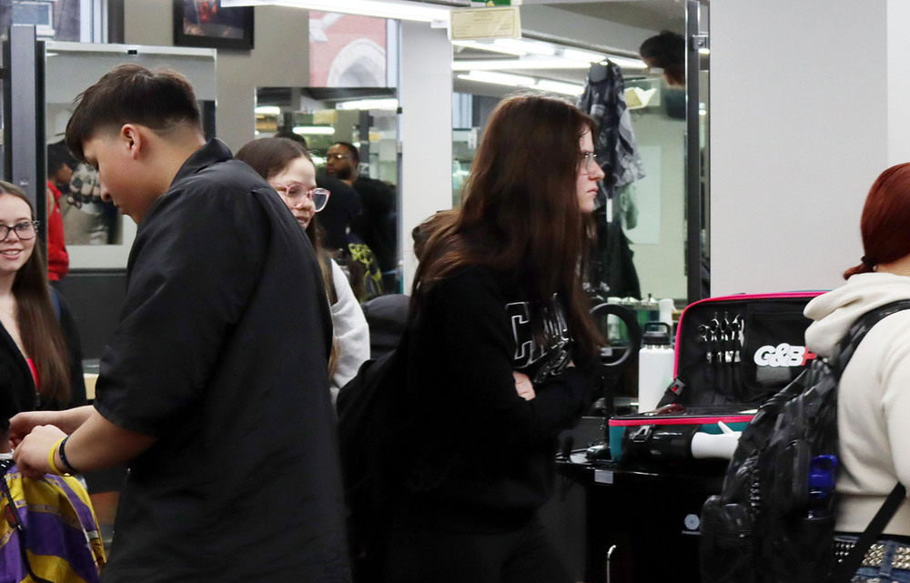 Four Bryan Community students walk through a hair salon as part of a field trip. A male barber is cutting a customer's hair on the lefthand side.