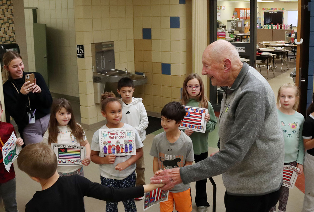 Several Fredstrom Elementary School students hold thank you signs as a veteran and his grandson walk past during a Veterans Day ceremony. A teacher is capturing the moment with her smartphone.