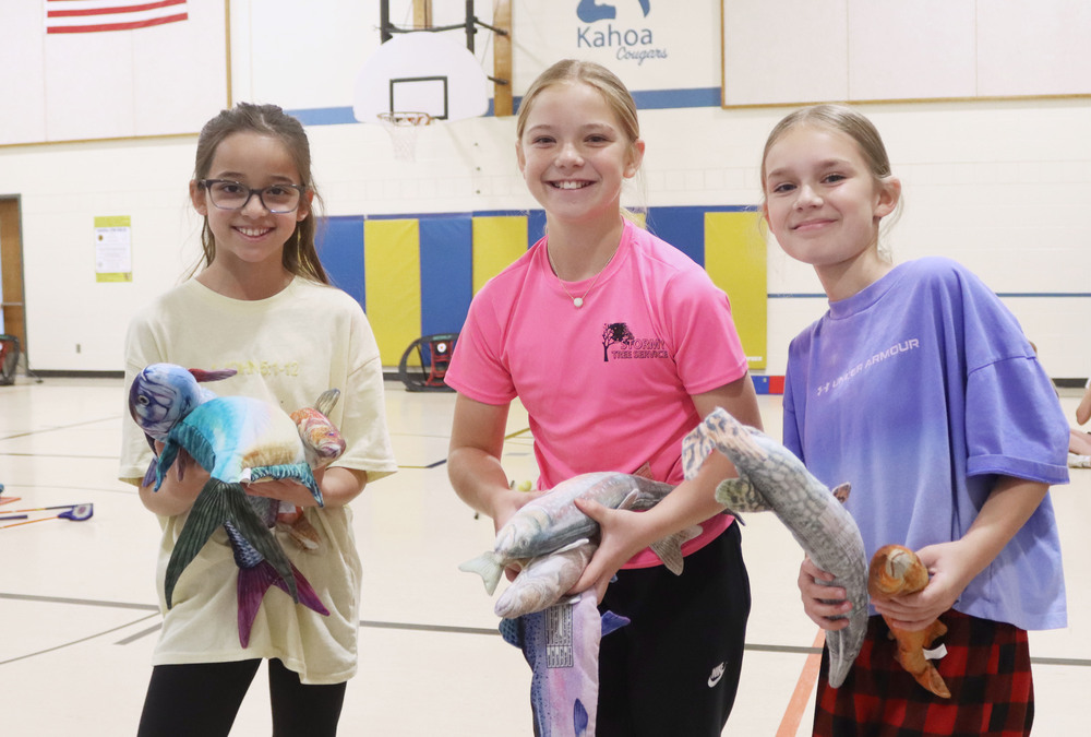 From left, Kahoa Elementary School fourth graders Nevaeh, Hadley and Keefer smile with stuffed fish they caught during a fishing lesson in their PE class. All three are holding several fish with both hands.