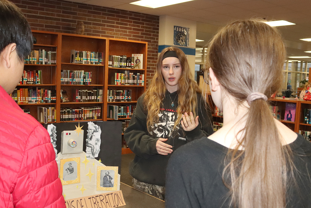 An East High School student explains her project to two fellow students in the school library. Her project shows a camera with three photos of African-American heroes of the Civil War Era.