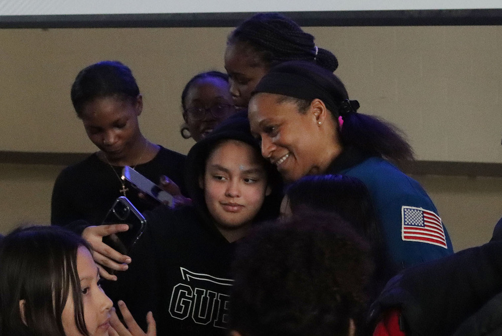 NASA astronaut Jeanette Epps stands next to a Goodrich Middle School student who is taking a selfie of them together. Five other students are gathered around them.