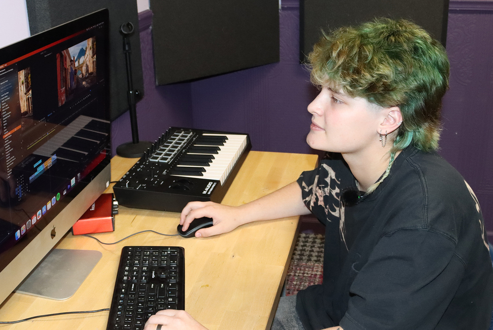 Bay High Focus Program senior Lexie works on a computer program in a Bay High Focus Program studio room. She is holding a mouse with her right hand and is typing on a keyboard with her left hand.