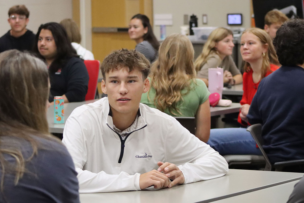 Eleven high school and college students practice their networking skills during UNL Accounting Day. They are facing each other and are talking at tables in a classroom.