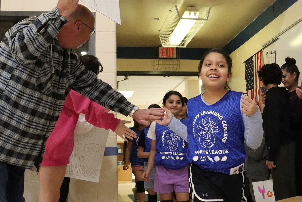 A Campbell Elementary School student receives a high five from a grandparent as she runs into the gym for a volleyball match. She is leading a line of teammates who are running through a tunnel of supportive family members.