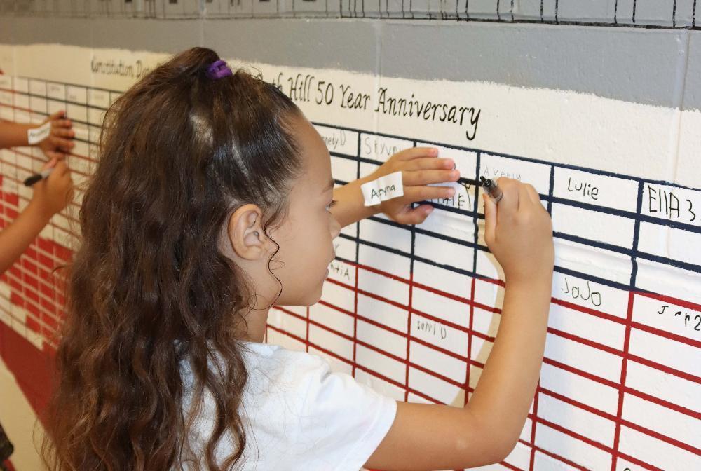 A Hill Elementary School student uses a black Sharpie pen to write her name on the wall of a Constitution Day display at the school.