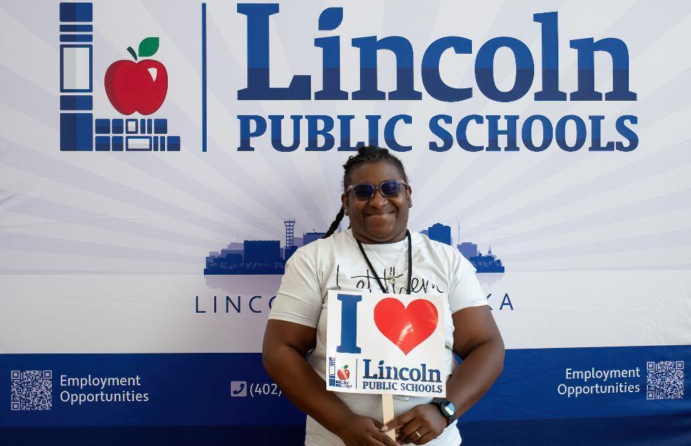 A new educator holds a sign that says I love Lincoln Public Schools while standing in front of a backdrop at a new educator orientation event.