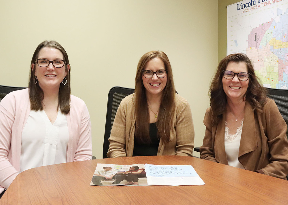 From left, Sara Stoner, Megan Lytle and Wendy Rau sit next to each other at a table in a conference room. There is a district map of Lincoln Public Schools on a side wall behind them. There is a copy of the research paper they produced laying on the table in front of them.