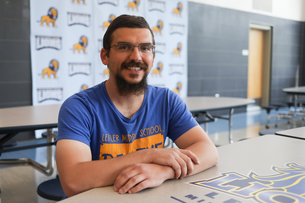 Man in blue shirt sits in a school cafeteria.