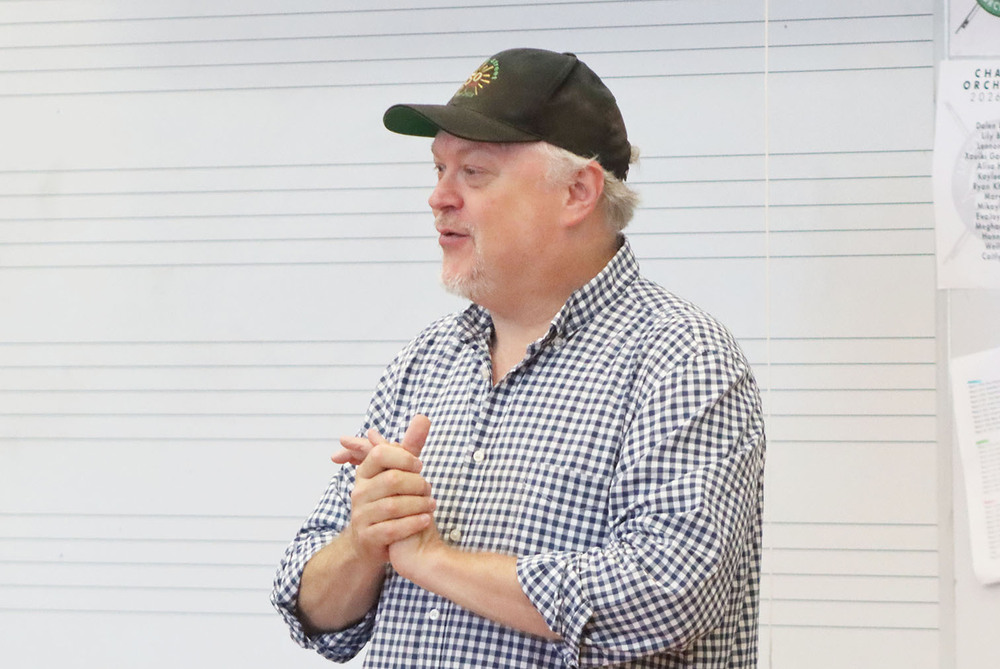Jazz at Lincoln Center Orchestra trumpet player Kenny Rampton smiles as he visits with Southwest High School students inside a music classroom. He is standing in front of a large whiteboard that has music lines on it.