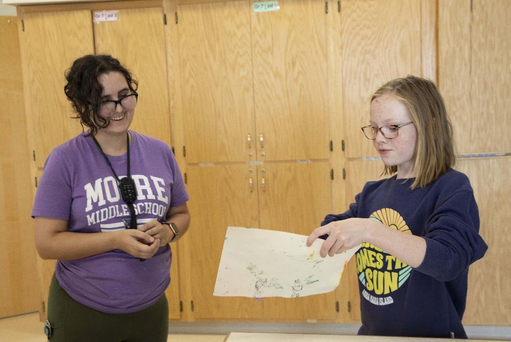 From left, Moore Middle School art teacher Kristen Douglas smiles at sixth grader Lilia as Lilia holds up her art project.