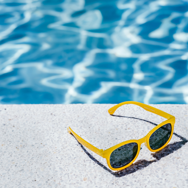 A pair of yellow sunglasses sitting at the edge of a swimming pool filled with water