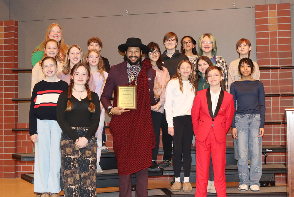 Sixteen Scott Middle School students stand with Ishma Valenti on stage during the school's Martin Luther King Jr. Day ceremony. Valenti is holding an award he received from the school for his community achievements.