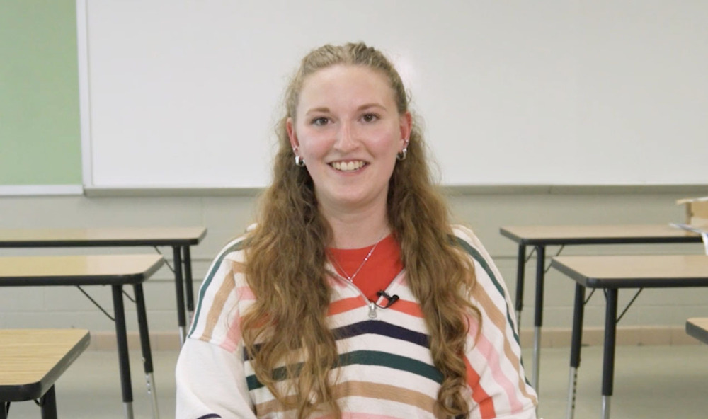 Dawes Middle School social studies teacher Zoey Snofski smiles in her classroom. She is sitting in the middle of a row of tables that students will be sitting in.
